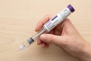 Mano sujetando pluma Mounjaro KwikPen de tirzepatida 5 mg lista para inyección subcutánea sobre superficie de madera